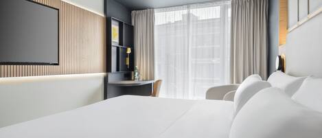 Une chambre d’hôtel moderne avec un grand lit, un bureau et un téléviseur fixé au mur.