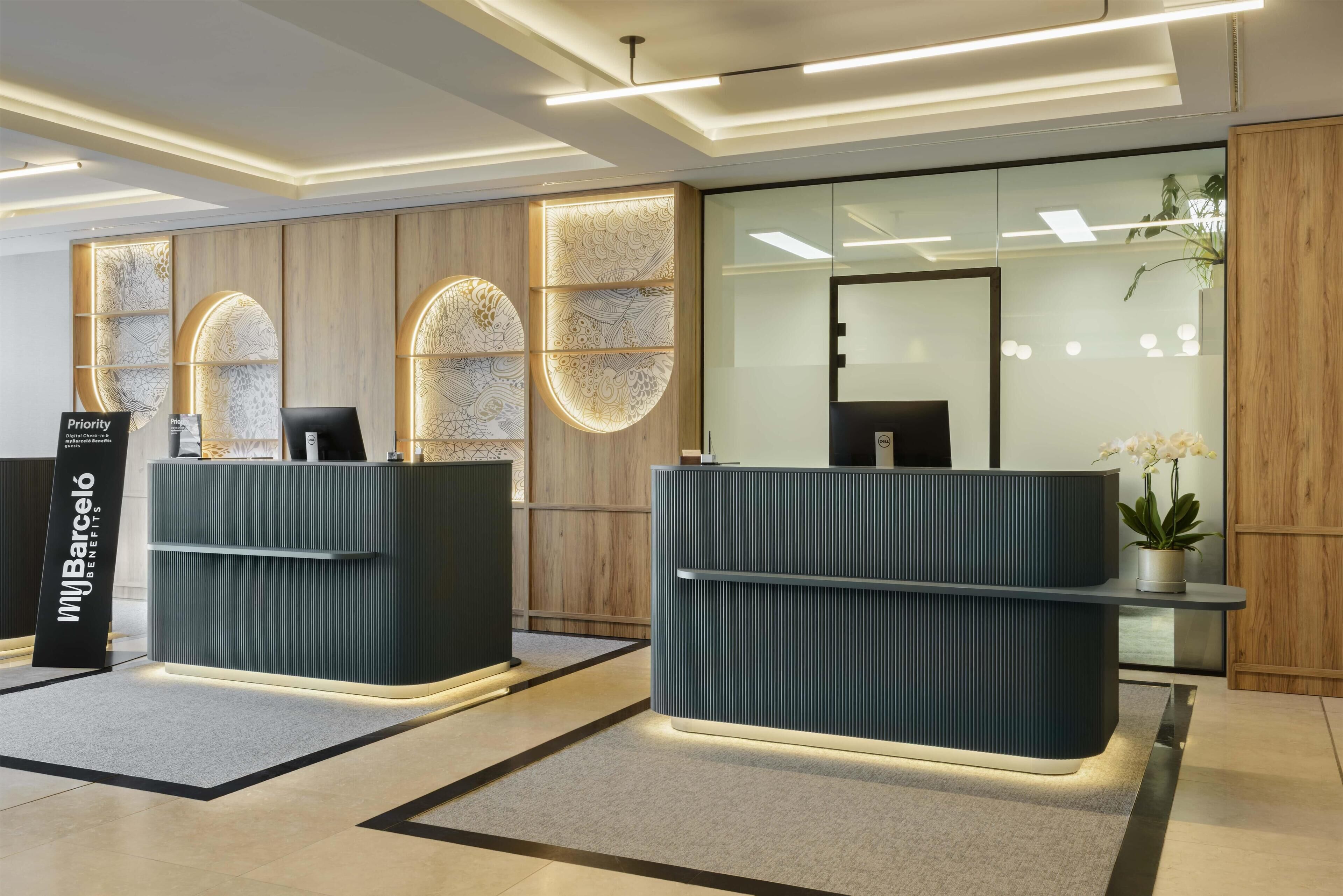 Un área de recepción con dos mostradores oscuros, una pared de madera con paneles decorativos y una planta en maceta.