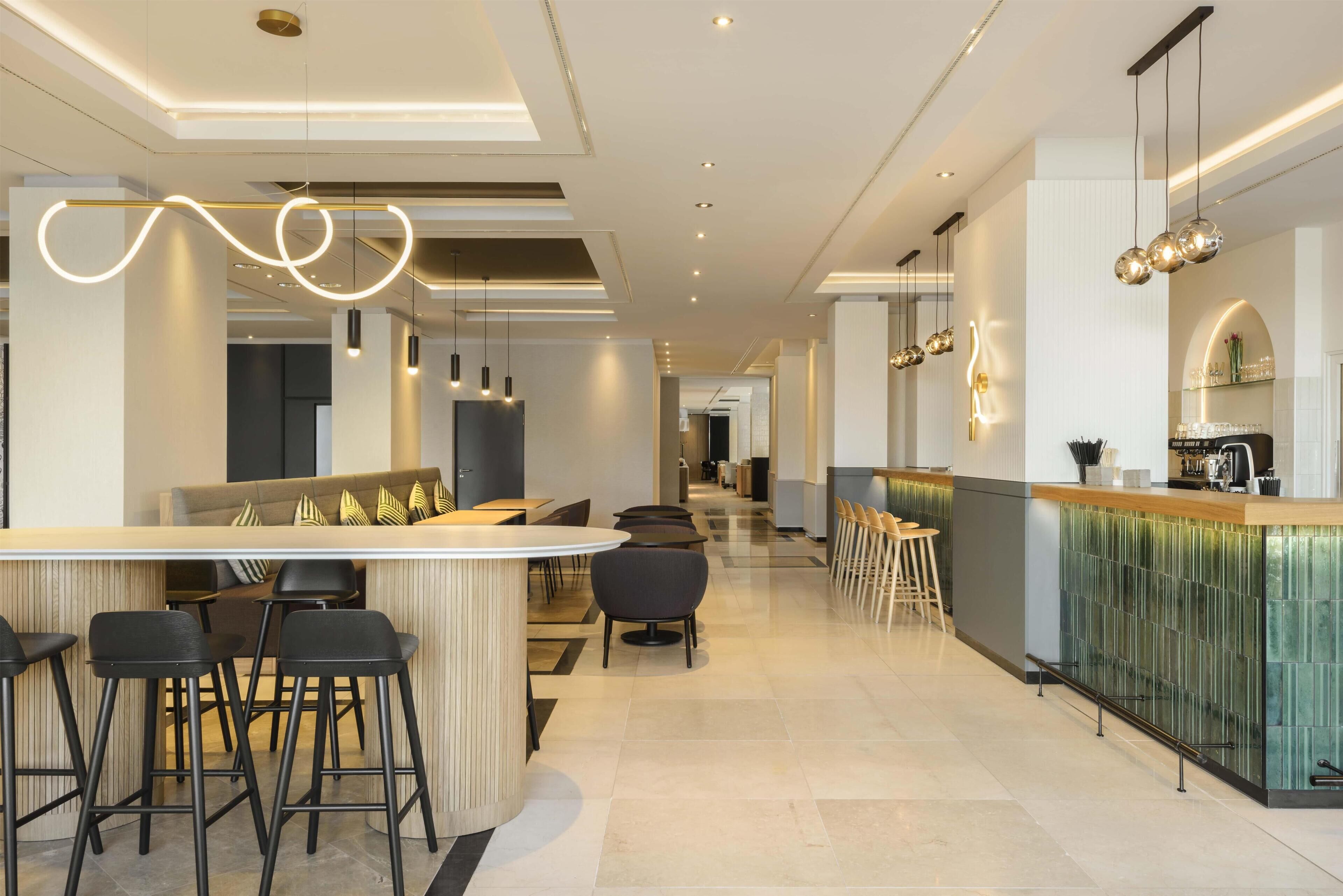 Una zona de bar moderna con taburetes altos, una barra larga e iluminación colgante.
