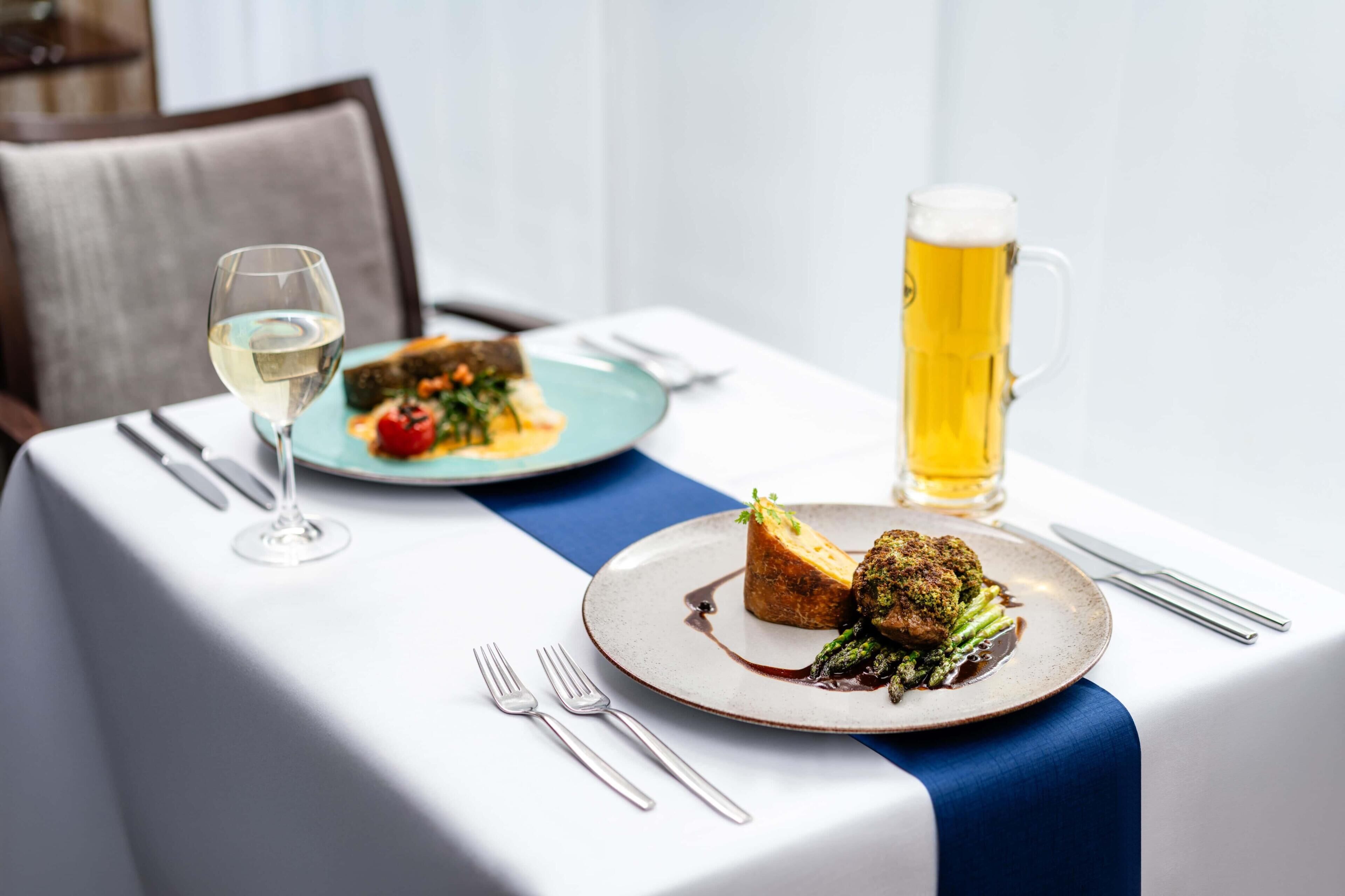 Ein Esstisch mit Speisen, einem Glas Weißwein und einem Bierkrug.
