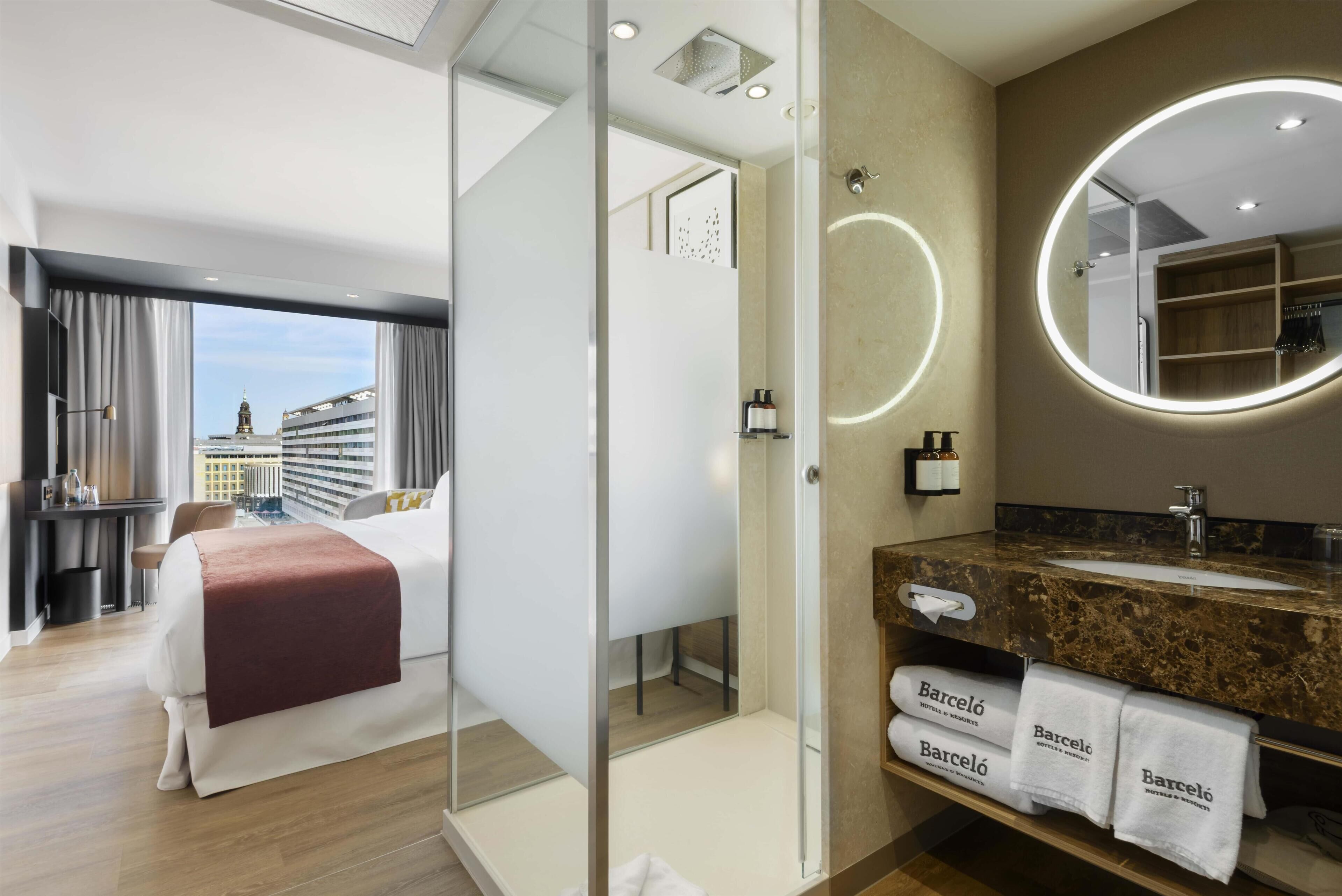 Una camera d'albergo con un letto, un bagno con uno specchio e vista sulla città.