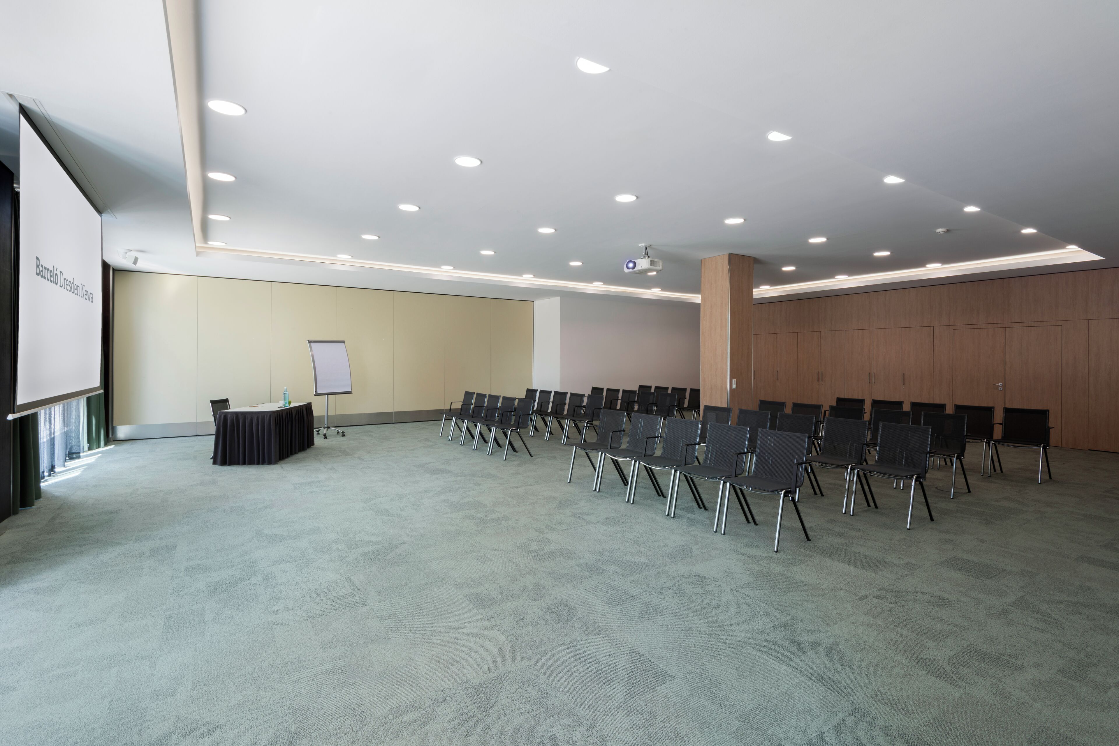 Une salle de conférence équipée d’une scène, d’un tableau blanc et de rangées de chaises.