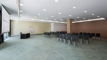 Une salle de conférence équipée d’une scène, d’un tableau blanc et de rangées de chaises.