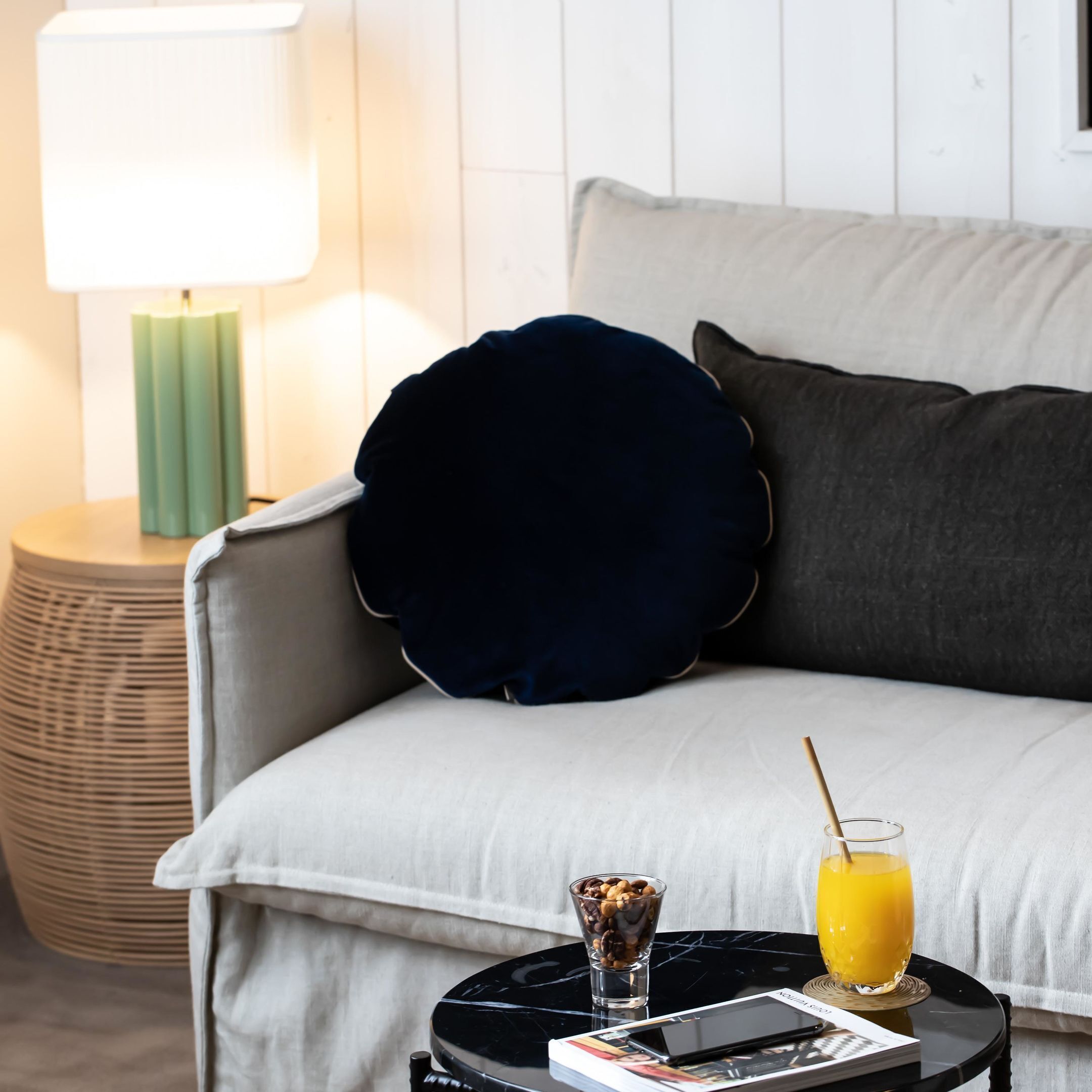 Ein modernes Wohnzimmer mit einer Couch, einem runden Beistelltisch, einer Lampe und einem Glas Orangensaft.