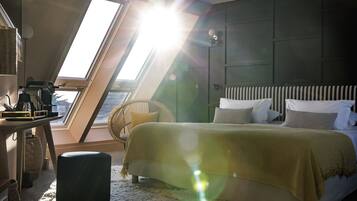 Un dormitorio con tragaluces, una cama con ropa de cama a rayas, una silla y una mesita de noche con lámpara.