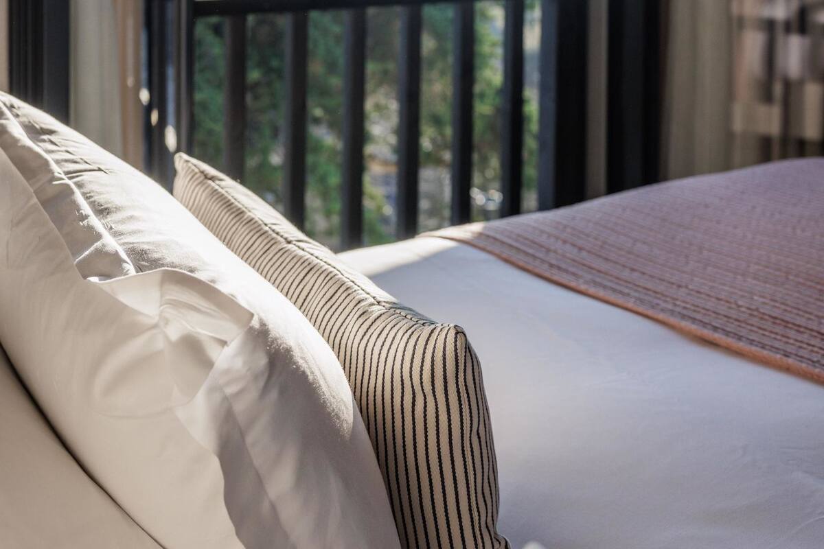A bedroom with a large window, a bed, and a view of greenery outside.