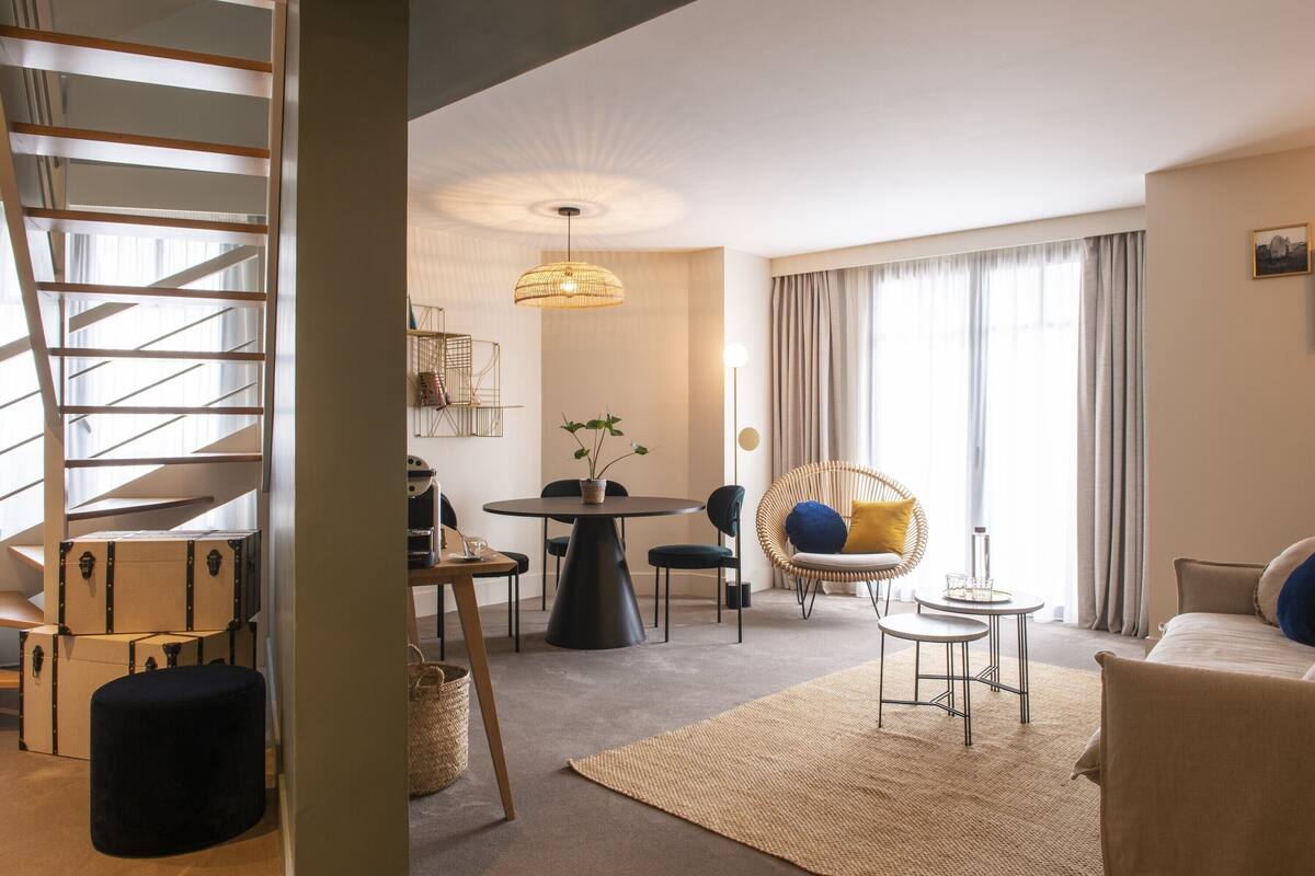A modern living room with a staircase, a round dining table, and a comfortable seating area.