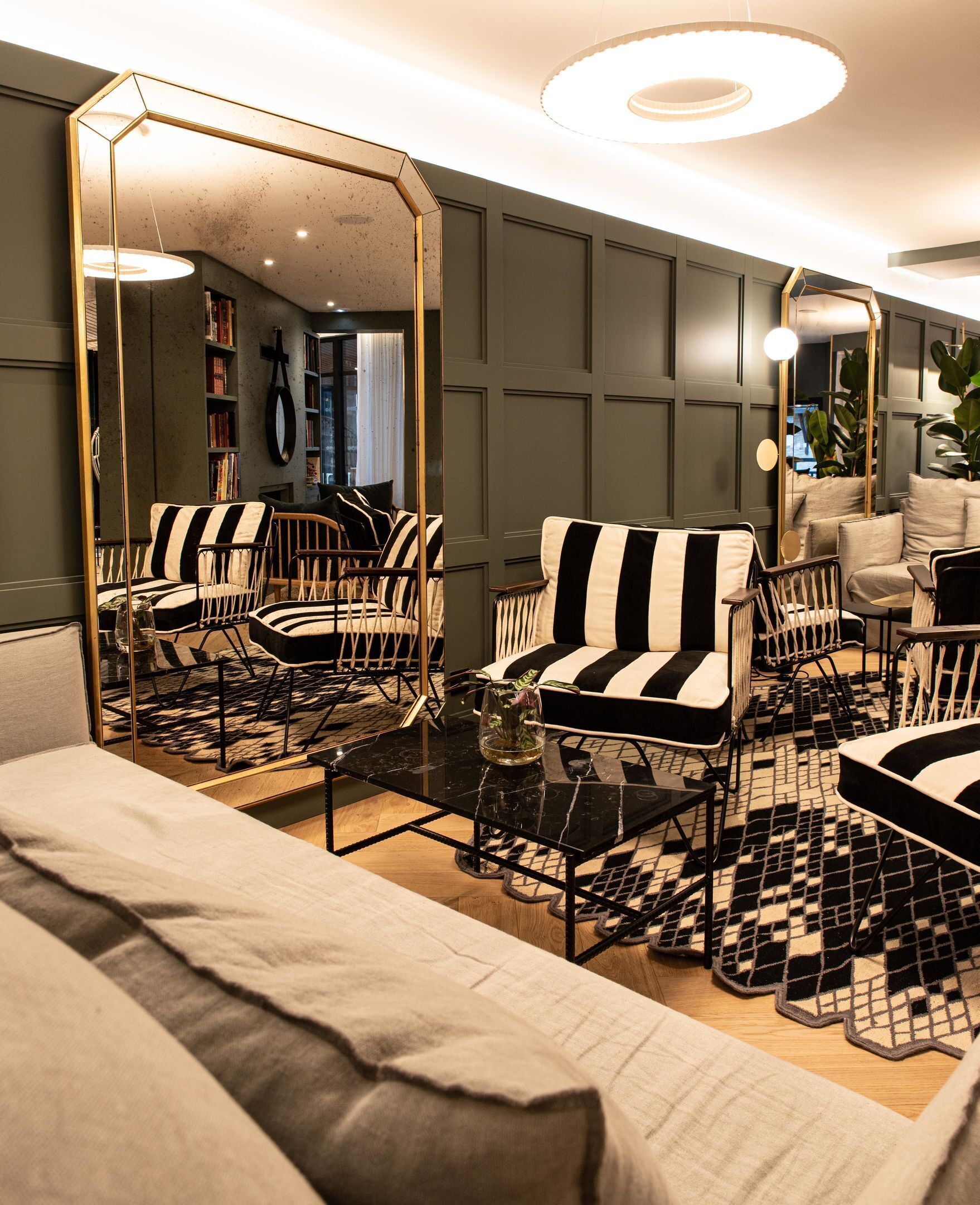 A modern living room with a sofa, armchairs, a coffee table, and a large mirror.