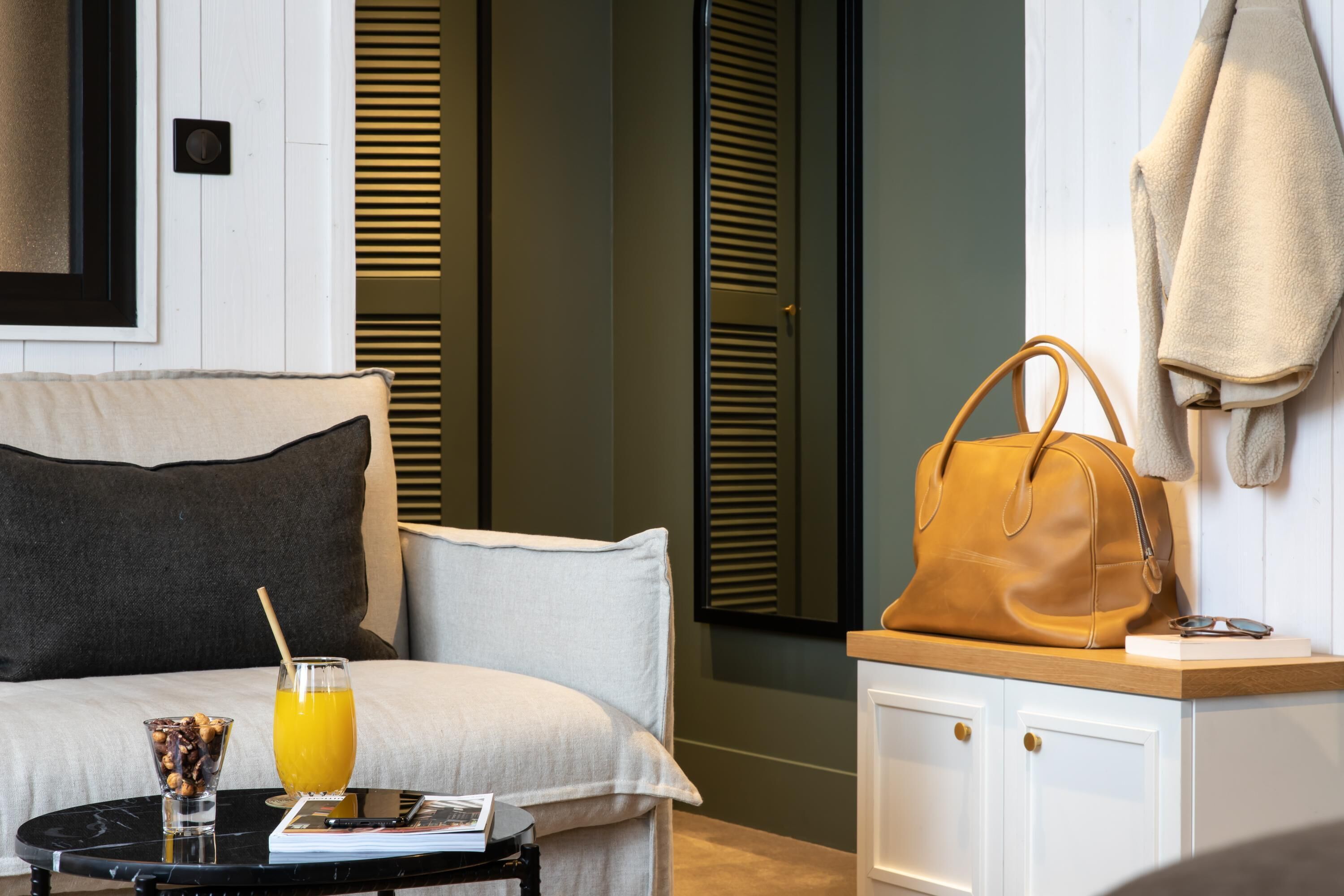 Een netjes ingerichte hotelkamer met een bed, een nachtkastje met een glas sinaasappelsap, een boek en een handtas op een klein tafeltje.