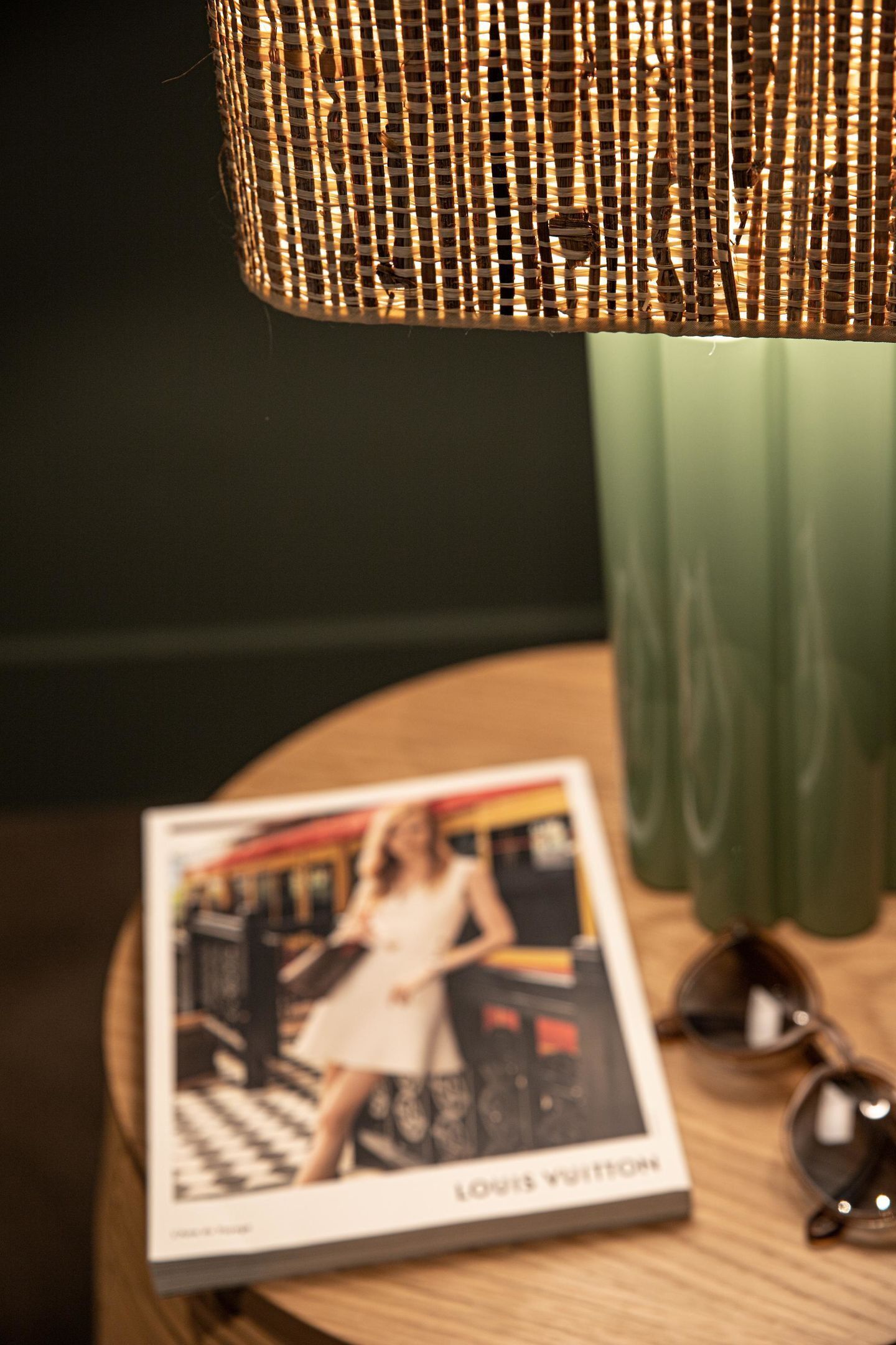 Un magazine posé sur une table en bois, avec une lampe en osier et un vase vert.