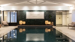 A modern indoor pool area with a stone wall, lounge chairs, and a sign reading "Le Celtique CARNAC". - Le Celtique & Spa (Carnac)