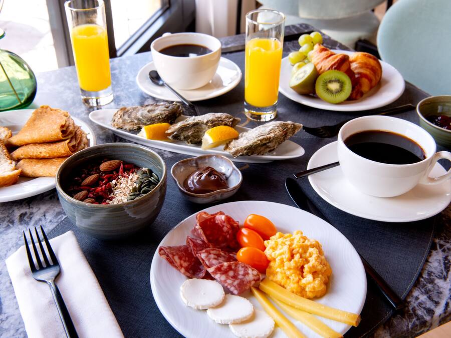 Una mesa de desayuno con diversos alimentos, como huevos, salchichas, queso y frutas.
