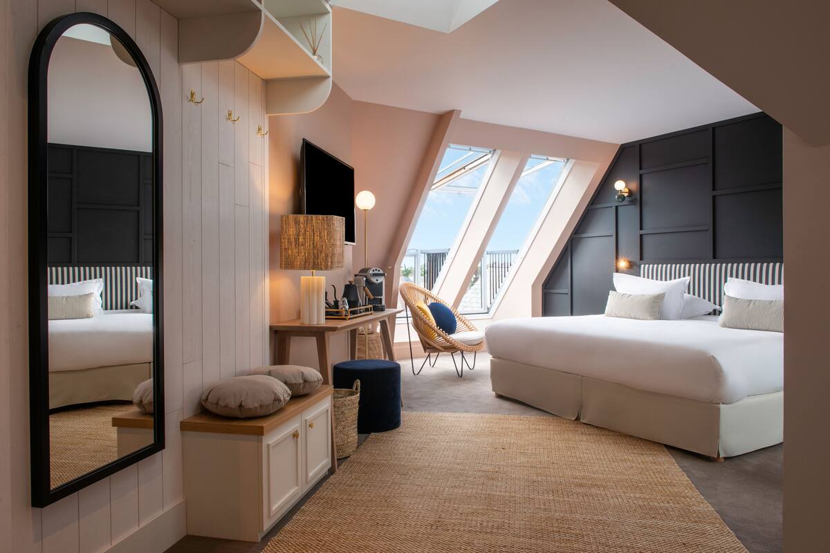 A modern bedroom with a large bed, a desk, a chair, a mirror, and a view through skylights.