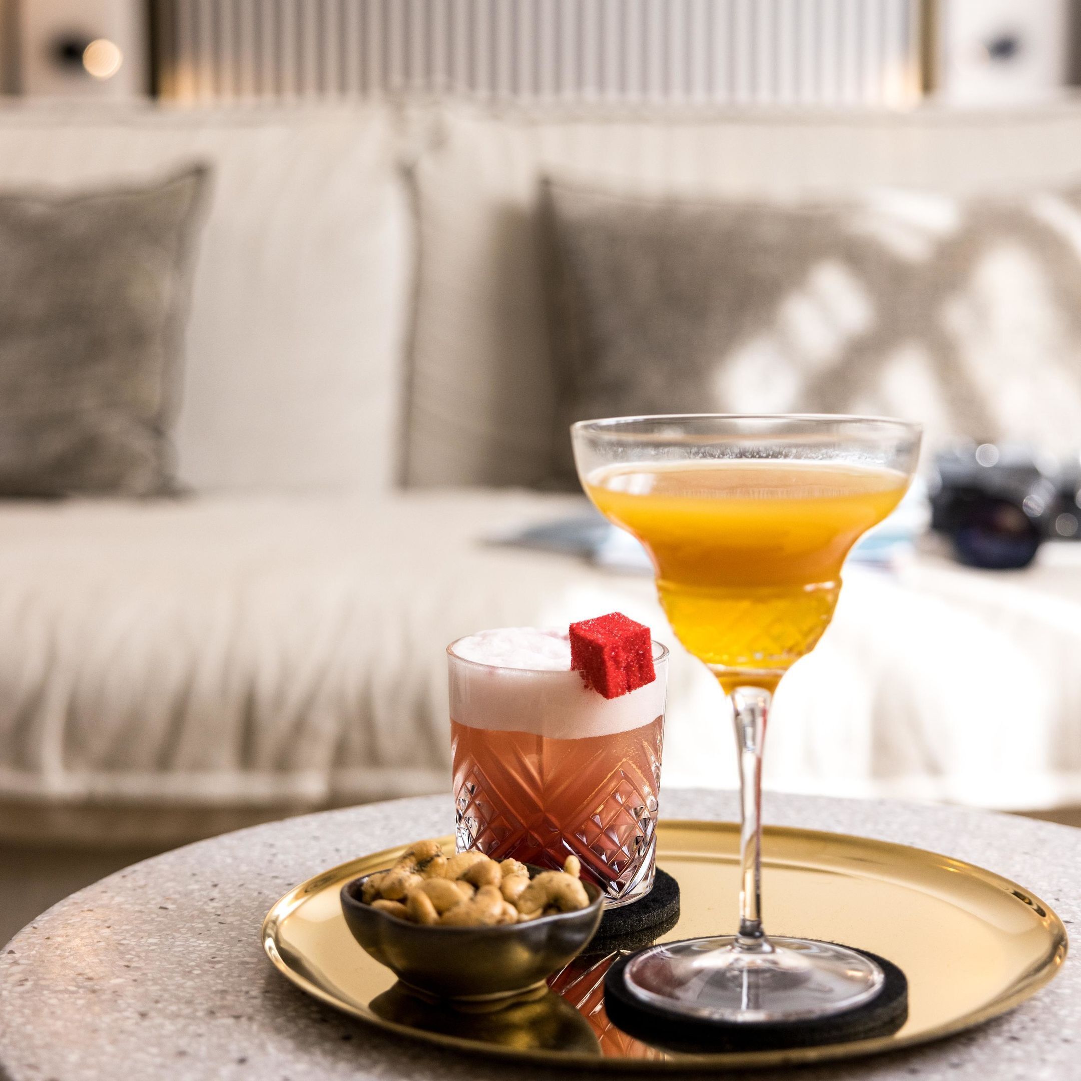 A martini glass with a red cube garnish and a cocktail in a glass with a textured pattern.