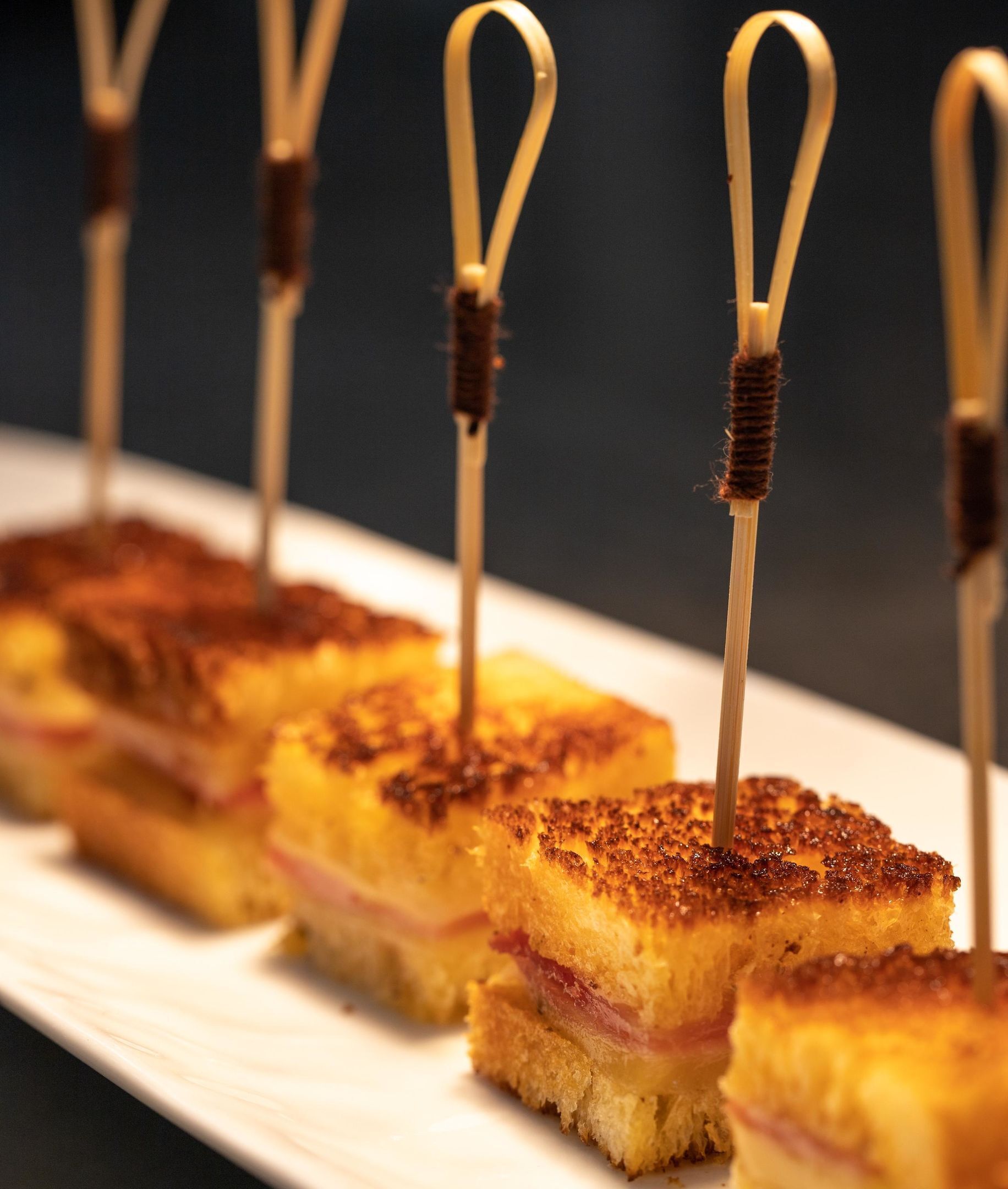 A series of square sandwiches with toothpicks, arranged on a white plate.