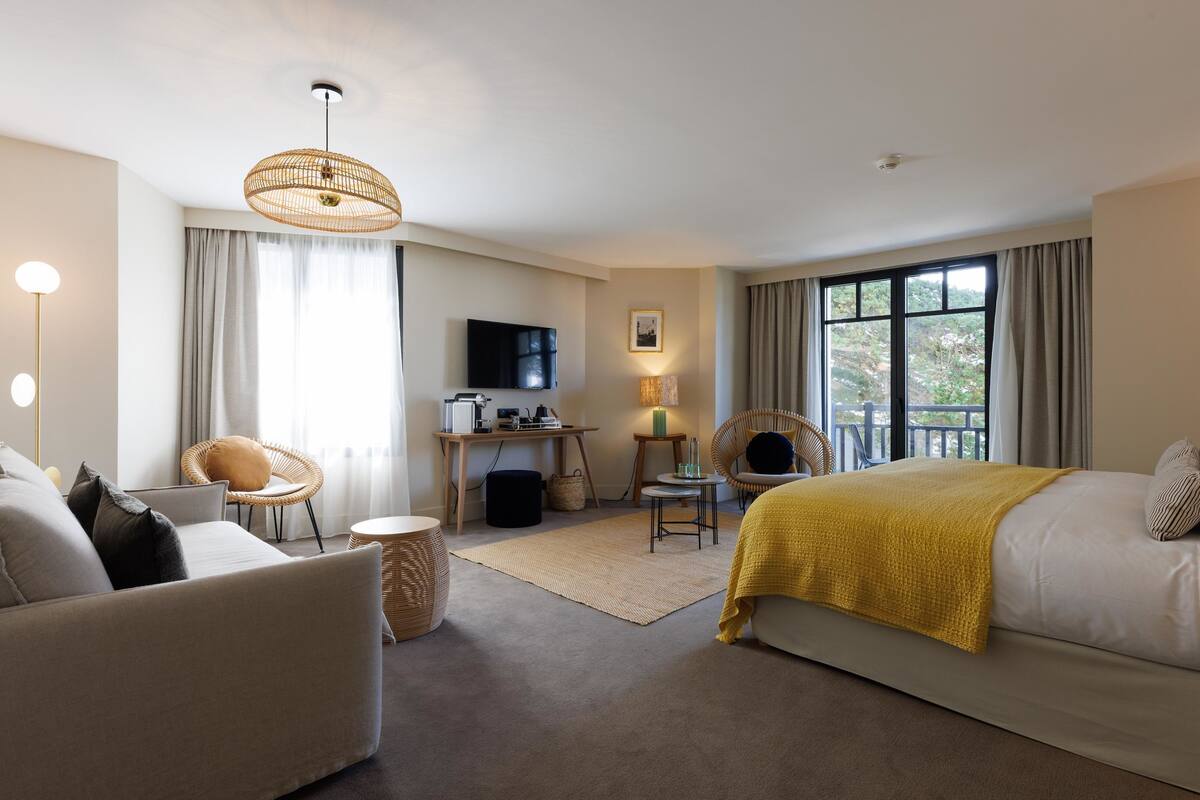 A hotel room with a bed, a sofa, a desk with a computer, a television, and a view of the outdoors.
