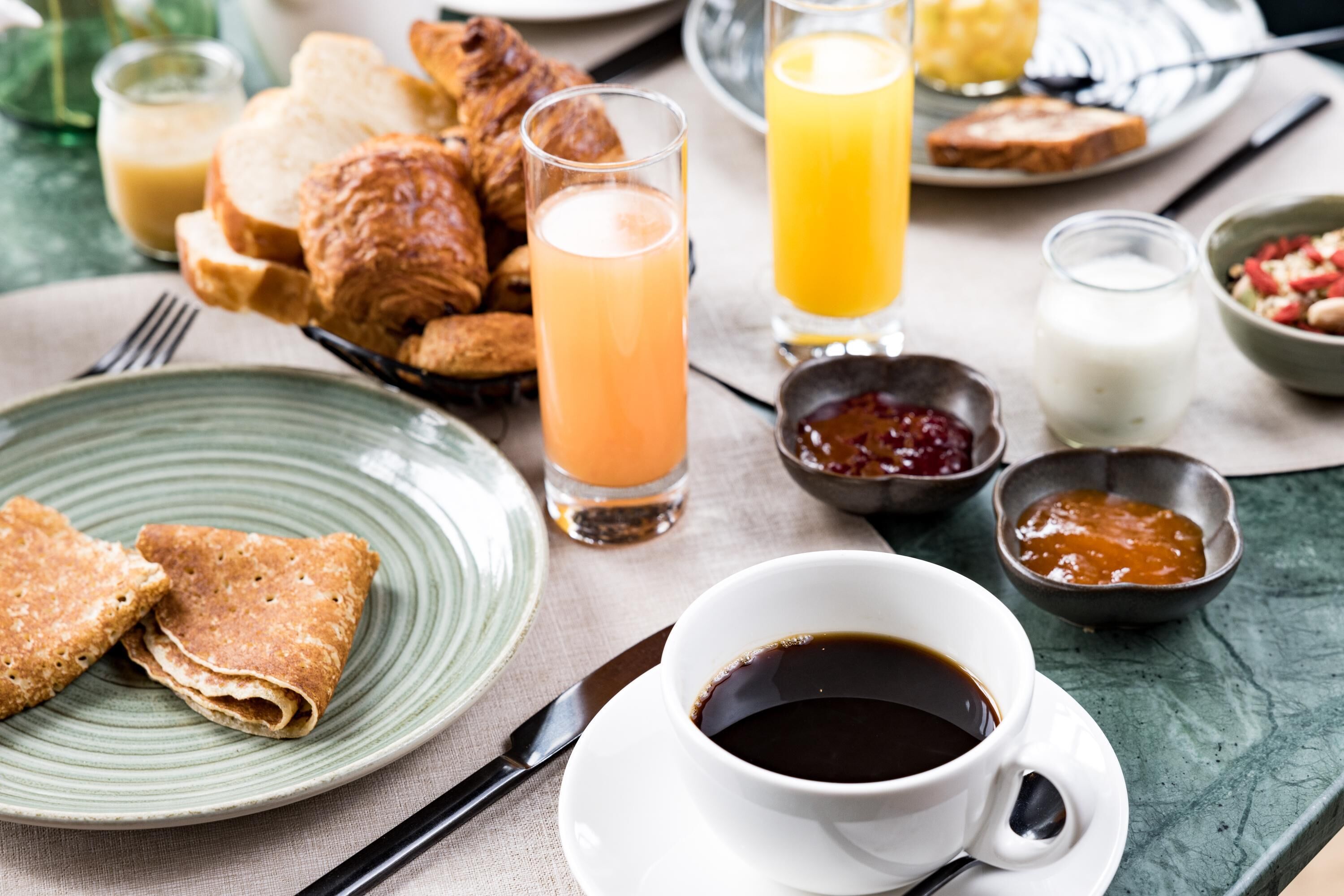 A breakfast setting with croissants, toast, juice, coffee, and jam.