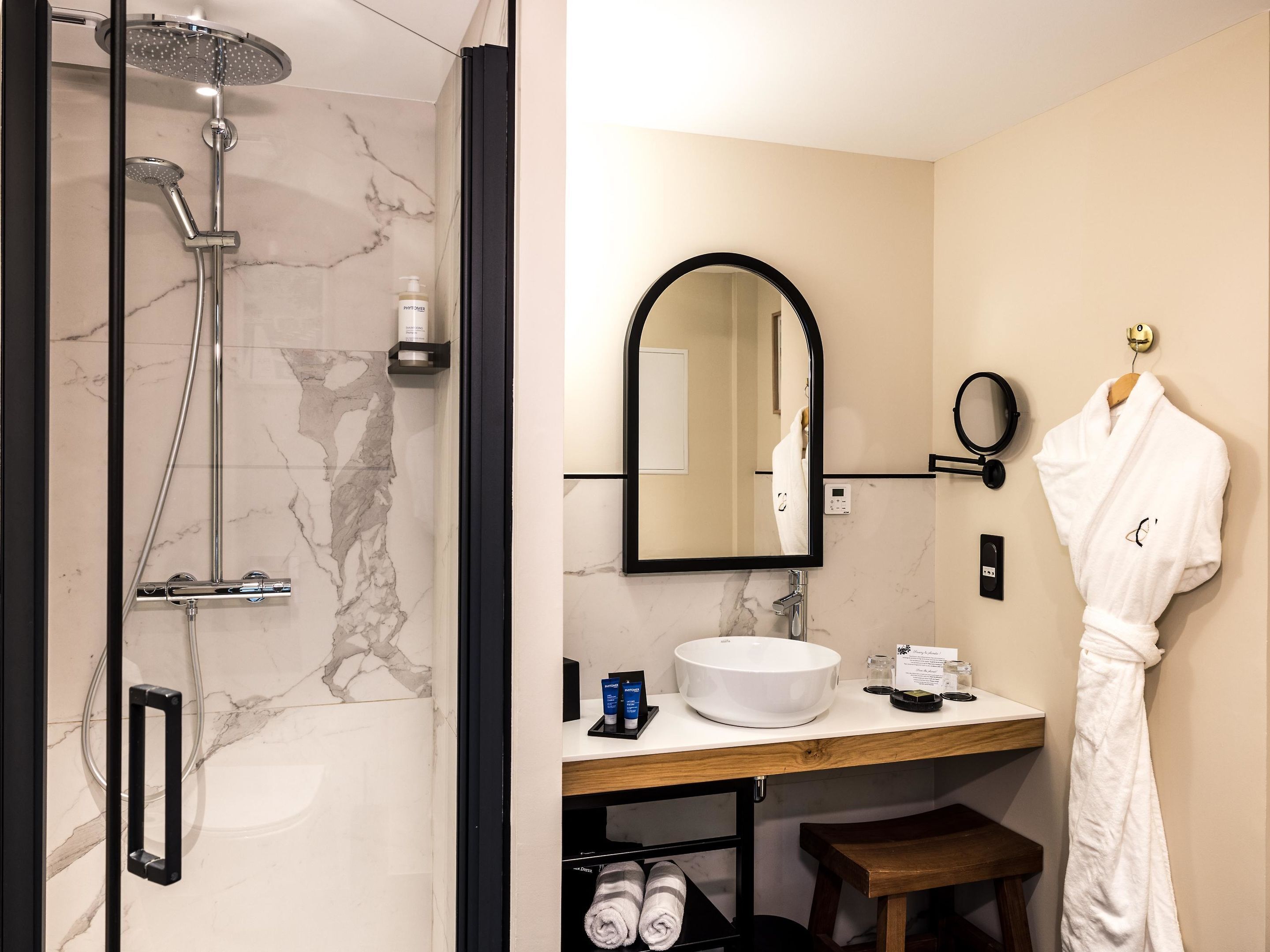 Une salle de bain moderne avec une douche en marbre, un grand miroir, un lavabo blanc et un peignoir suspendu à un porte-serviettes.