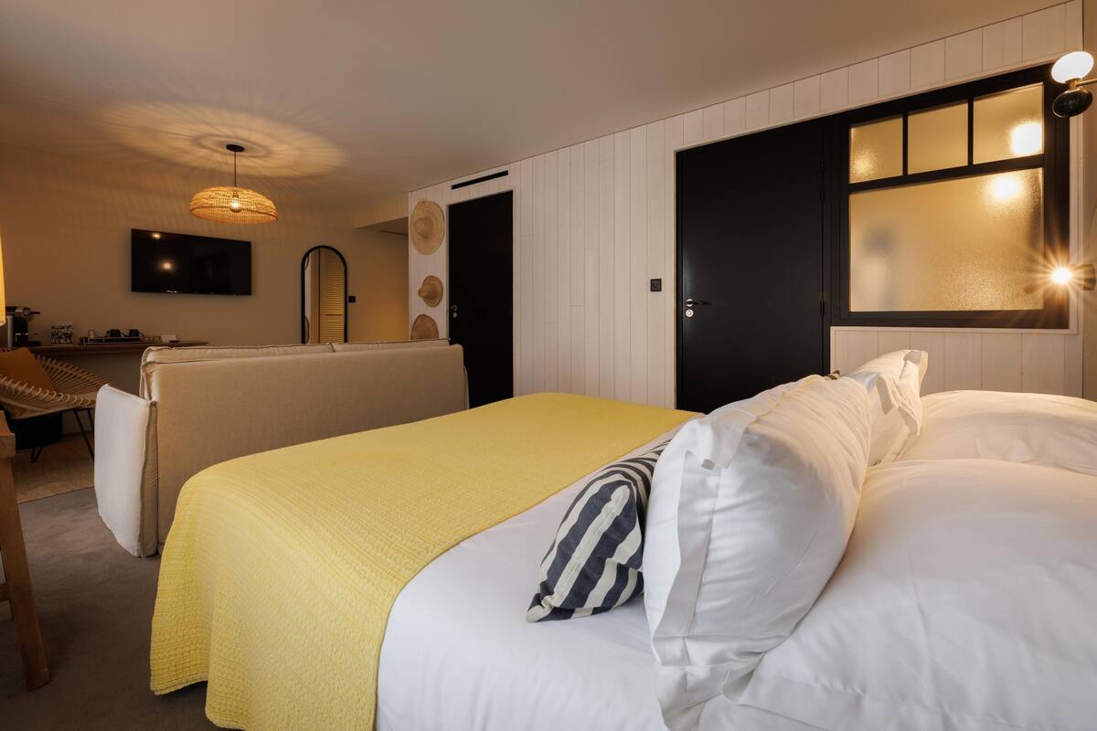 A hotel room with a bed, a sofa, a television, and a desk with a lamp.