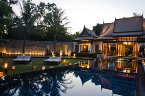 A poolside area with lounge chairs, a stone wall, and a building with traditional architecture. - Banyan Tree Phuket (Choeng Thale)