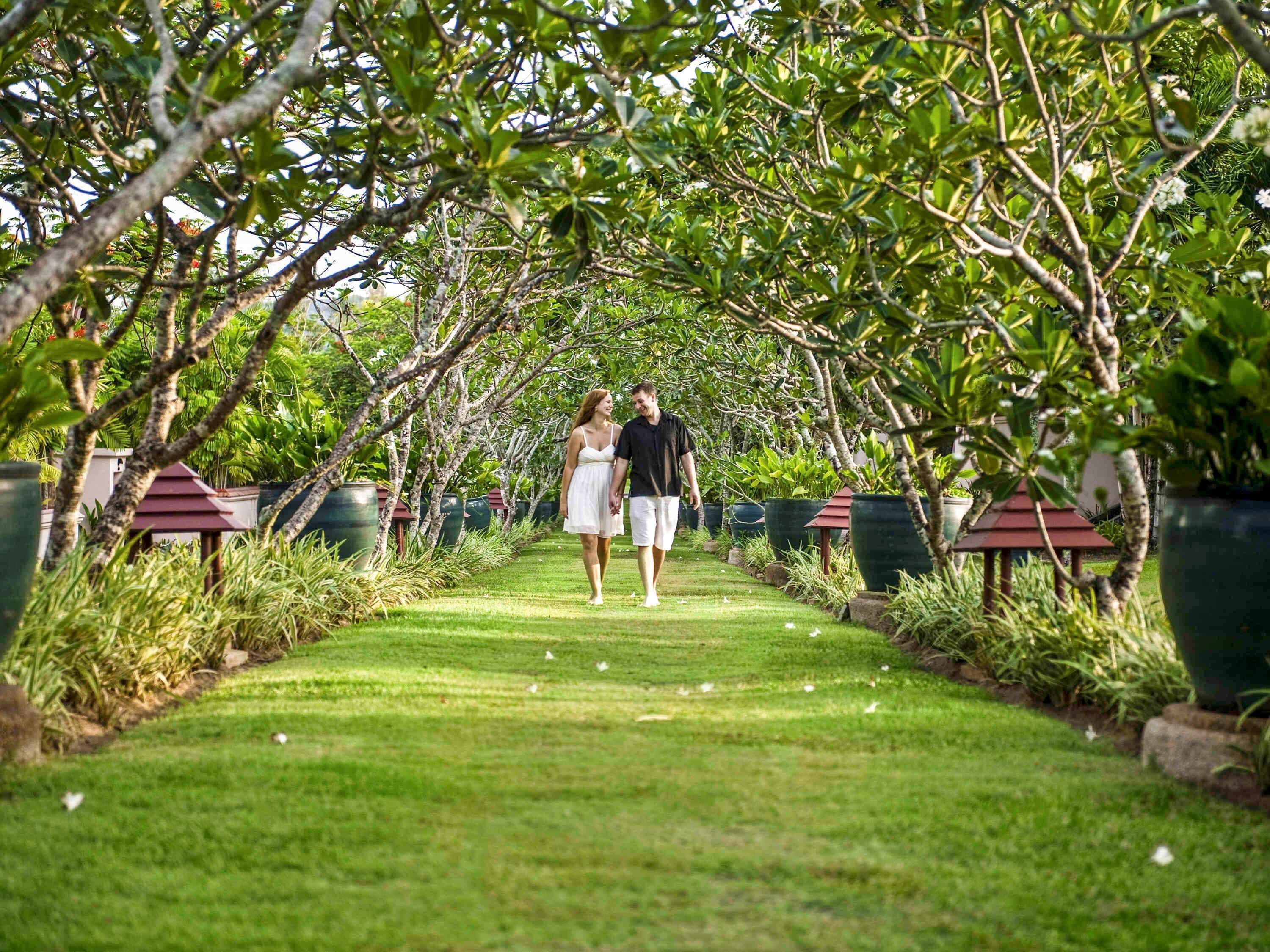 A pathway lined with trees and potted plants, leading to a gazebo.