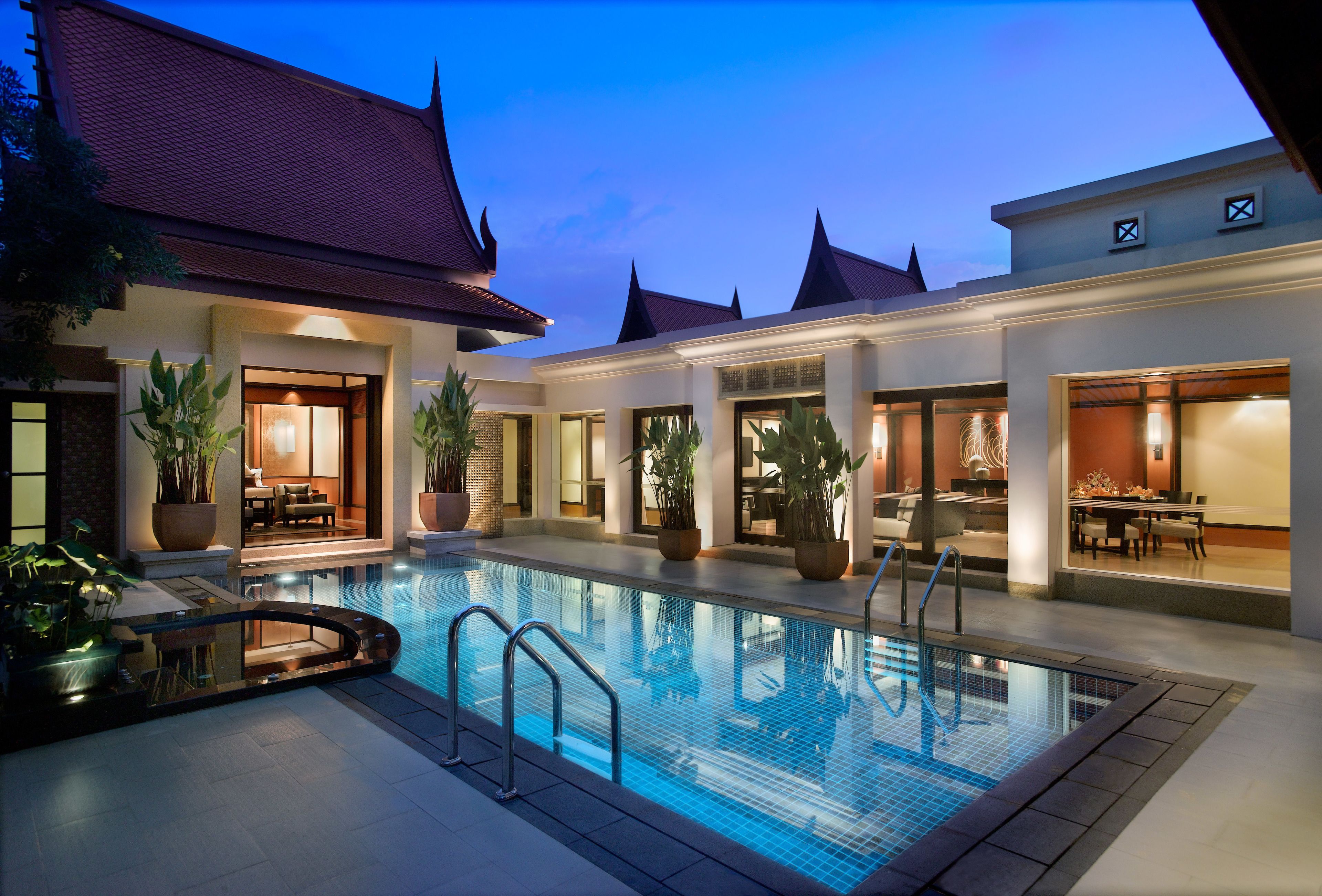 A swimming pool with a glass border, surrounded by potted plants and outdoor seating areas.