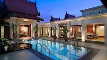 A swimming pool with a glass border, surrounded by potted plants and outdoor seating areas.
