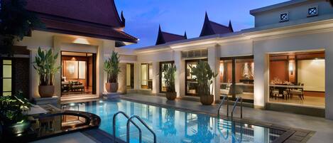 A swimming pool with a glass border, surrounded by potted plants and outdoor seating areas.