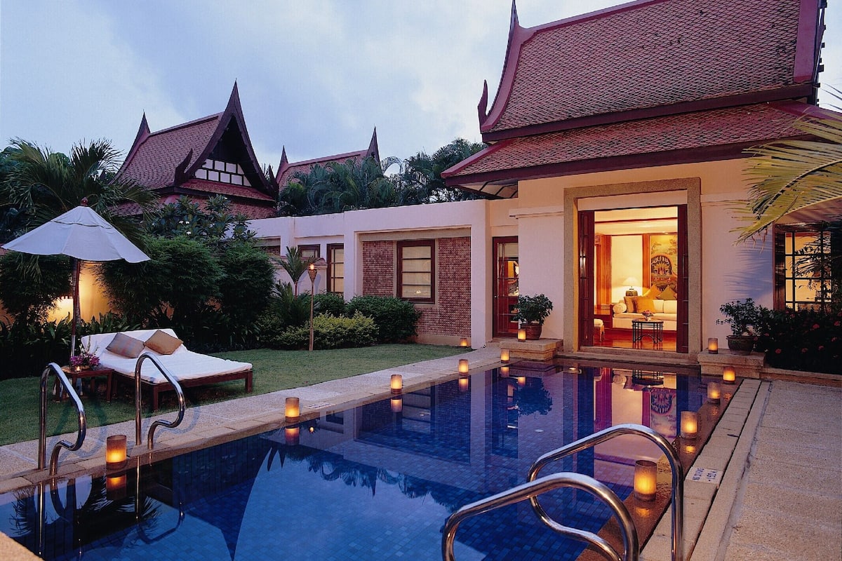 A swimming pool with a traditional architectural style, surrounded by a well-maintained garden and a building with a tiled roof.
