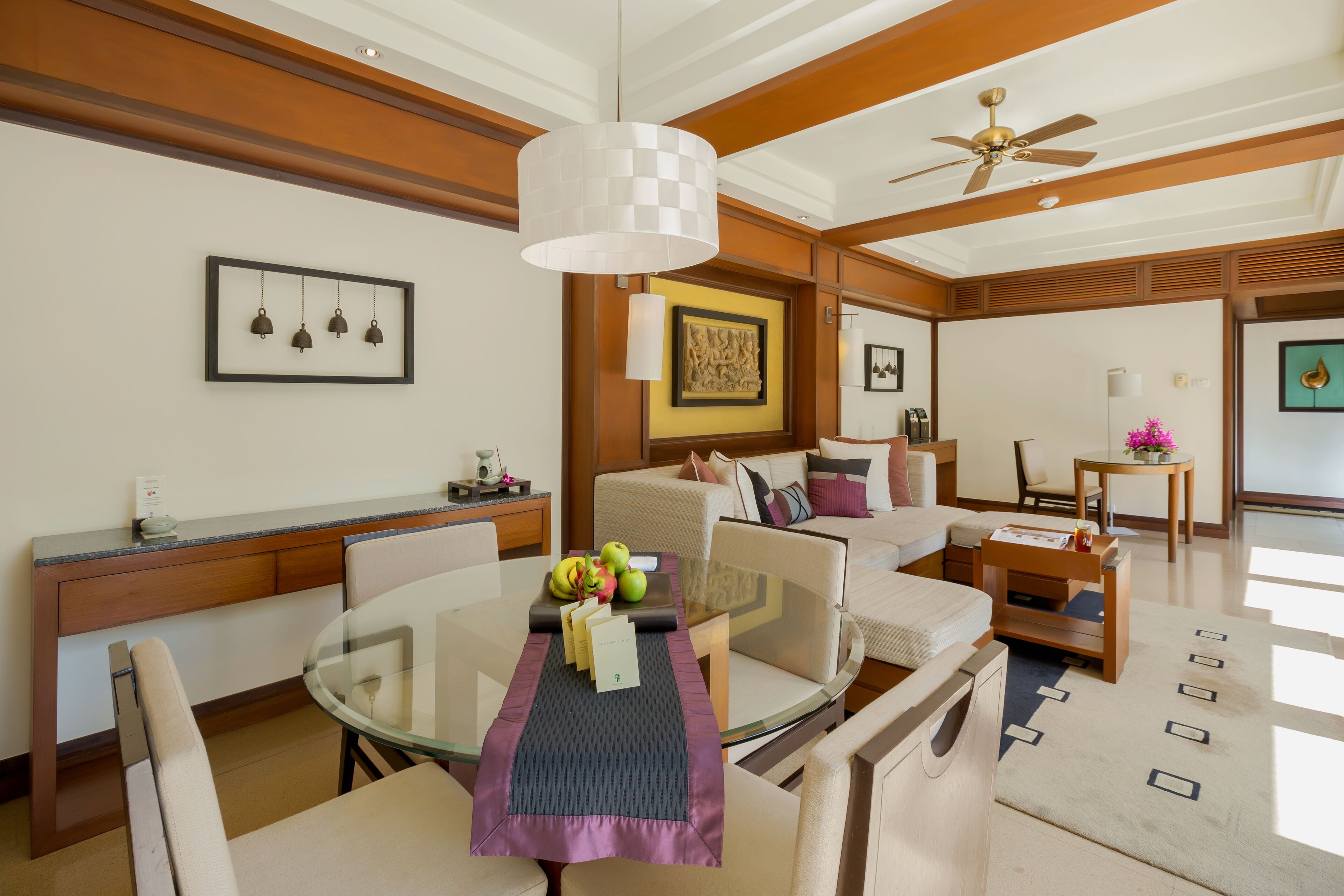 Una moderna camera d'albergo con zona pranzo, divano e ventilatore a soffitto, oltre a un quadro appeso al muro.