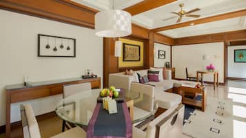 A modern hotel room with a dining area, a sofa set, a ceiling fan, and a framed artwork on the wall.