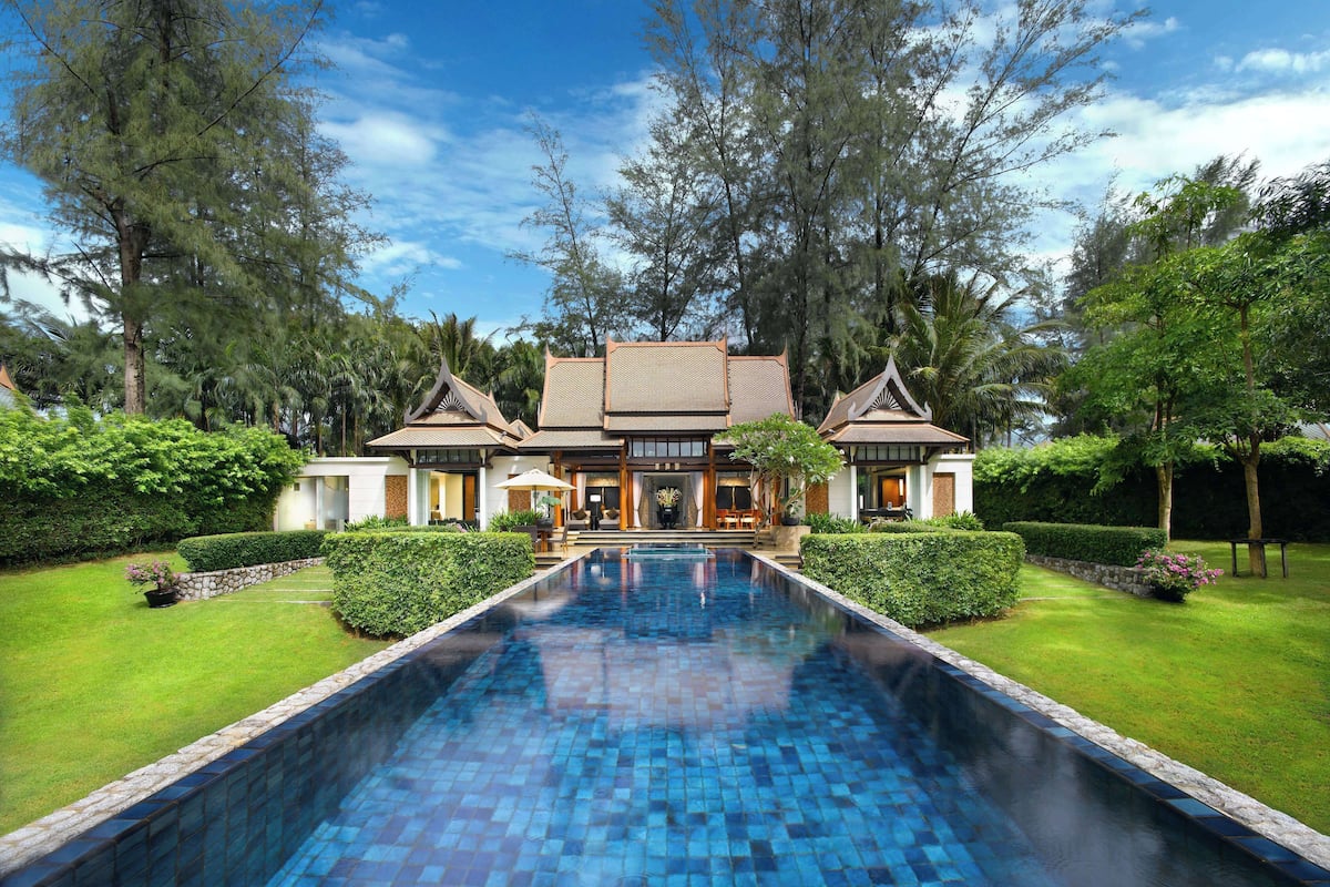A large house with a swimming pool, surrounded by lush greenery and trees.