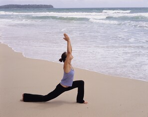A person performing a yoga pose on a beach with waves in the background.