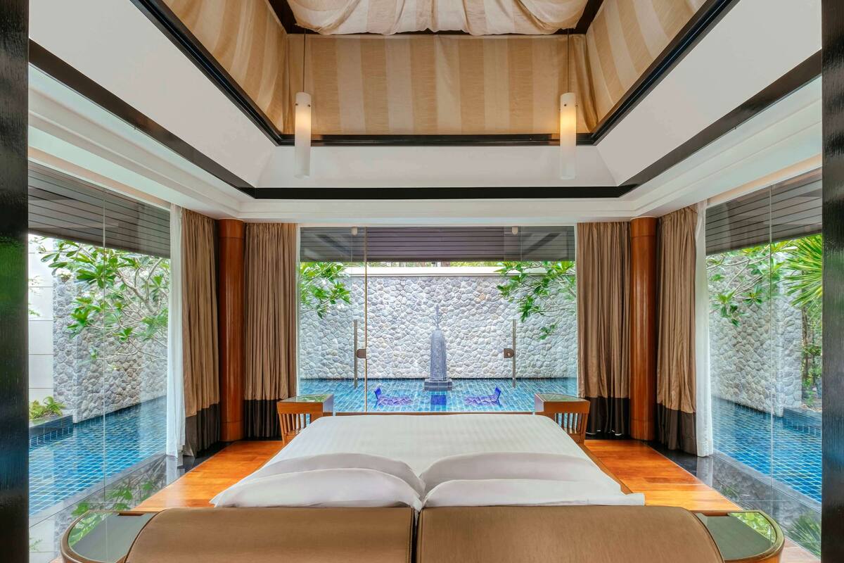 A spacious room with a large bed, a view of a swimming pool, and a stone wall.