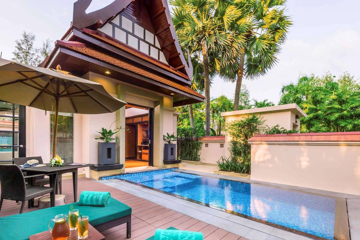 A modern outdoor pool area with a wooden deck, lounge chairs, and a covered seating area.