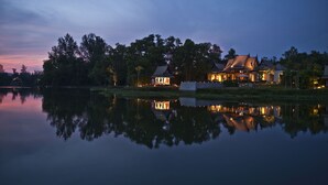 A lakeside property with multiple buildings, including a main house and smaller structures, reflecting on the water. - Banyan Tree Phuket (Choeng Thale)