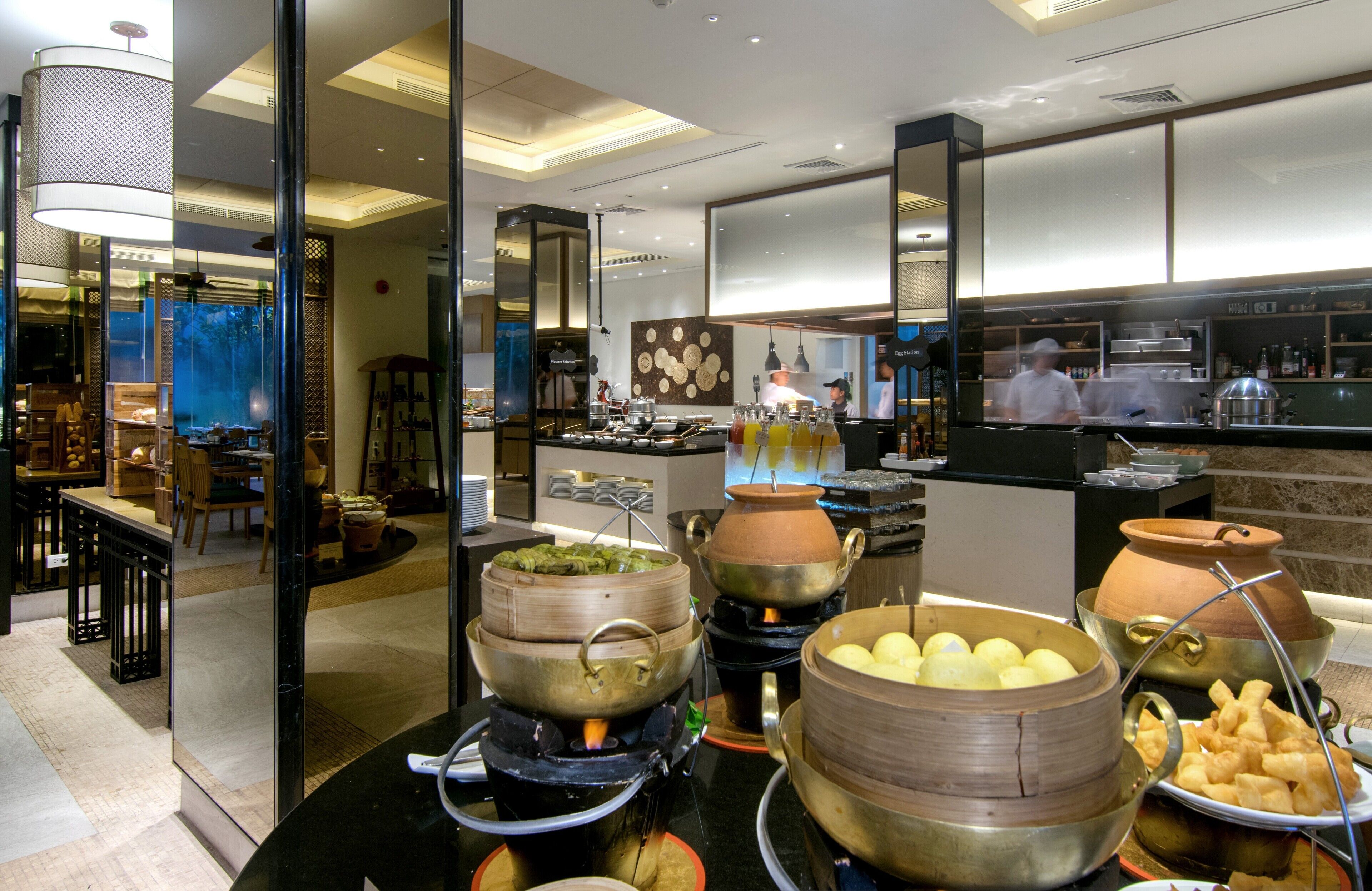 A modern restaurant with a buffet setup featuring various cooking stations and dishes.