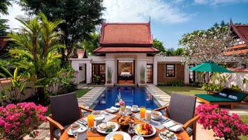 Un coin petit-déjeuner aménagé au bord de la piscine, avec une table, des chaises et une variété de plats et de boissons.