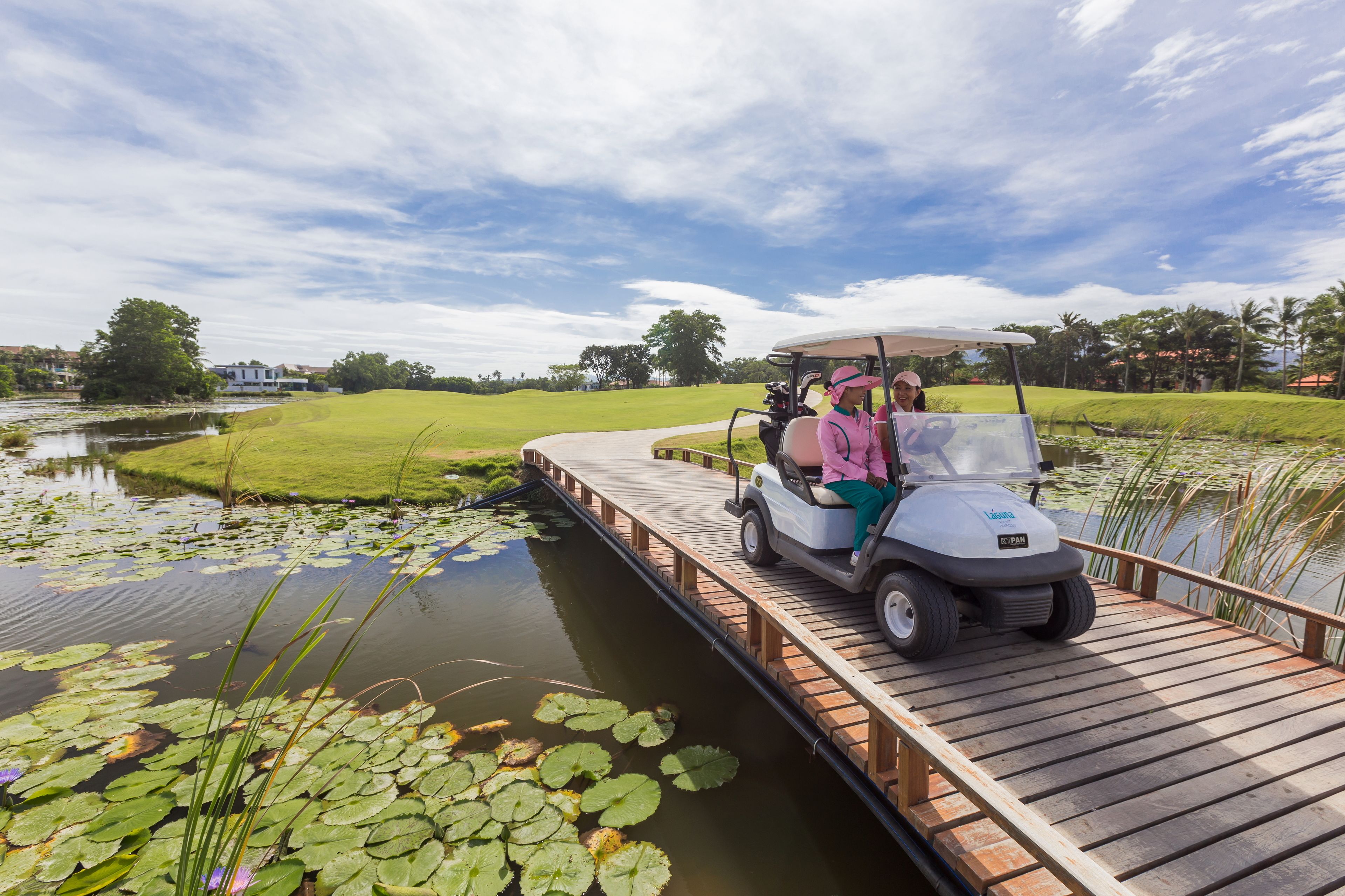 A golf cart on a wooden bridge over a pond with lily pads.