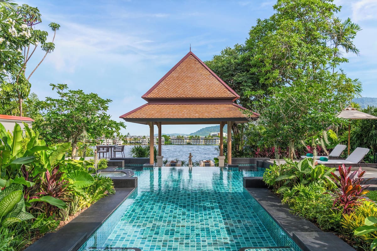 A swimming pool with a gazebo, surrounded by lush greenery and overlooking a body of water.