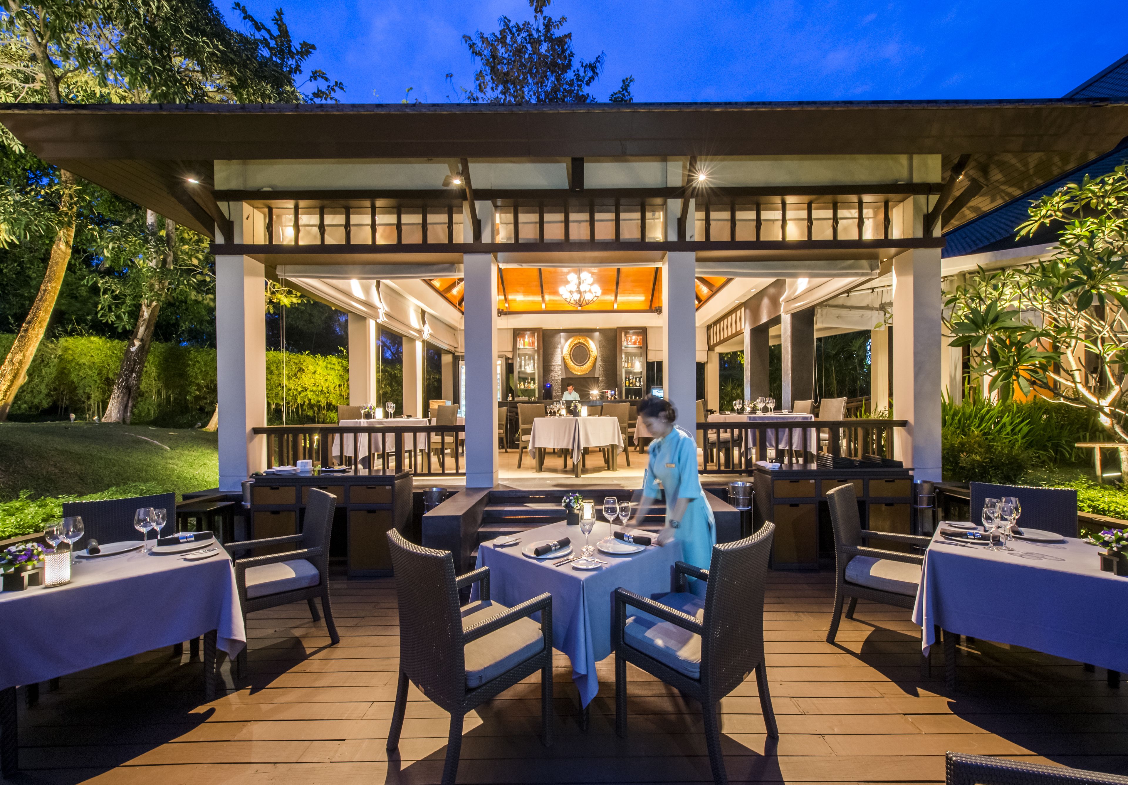 An outdoor dining area with tables and chairs, a waiter, and a covered section with a chandelier.