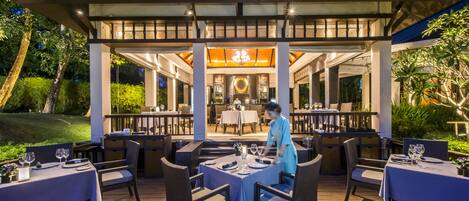 An outdoor dining area with tables and chairs, a waiter, and a covered section with a chandelier.