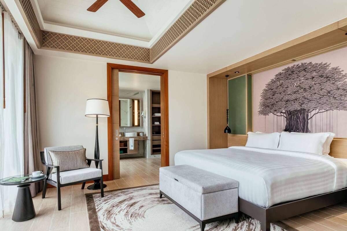 A modern bedroom with a large bed, a bedside table, a chair, and a floor lamp.
