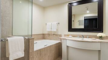 A bathroom with a glass shower enclosure, a bathtub, a sink with a mirror, and a vase with flowers.