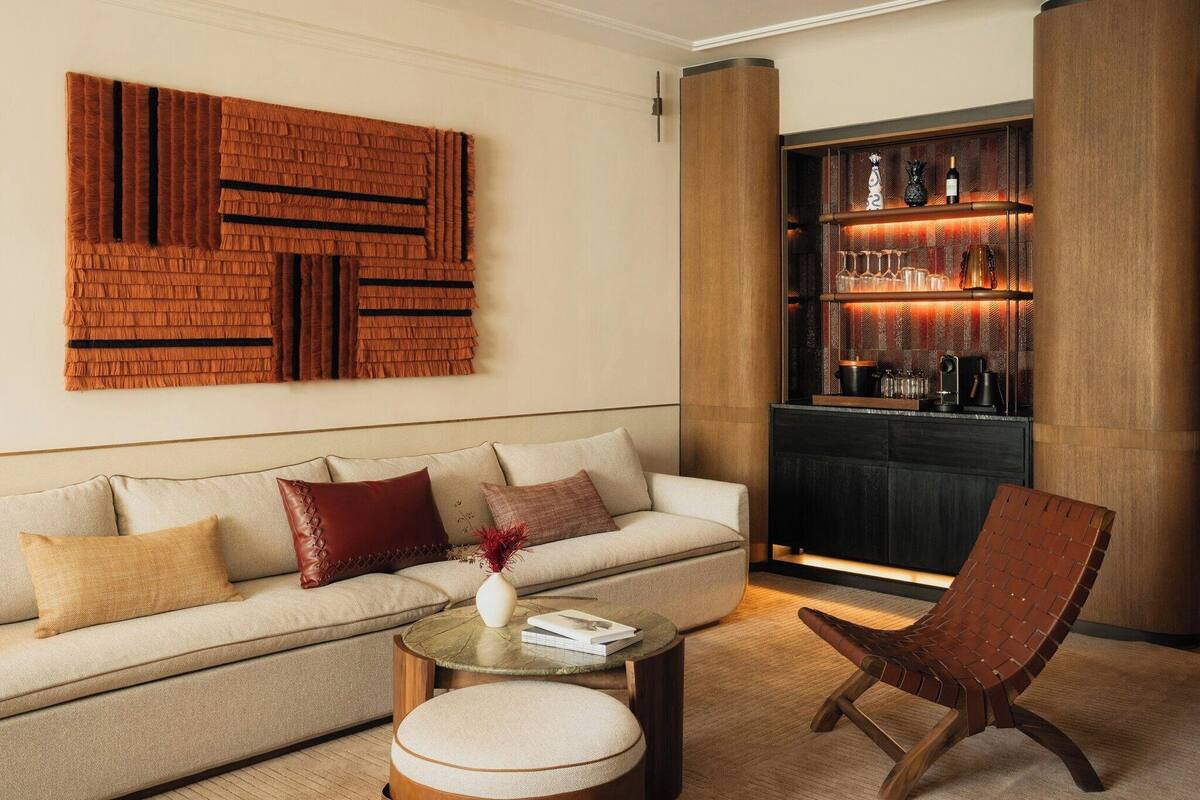 Una sala de estar moderna con un sofá, una mesa de centro y un sillón. Se aprecia una estantería empotrada con adornos y un alto pilón.