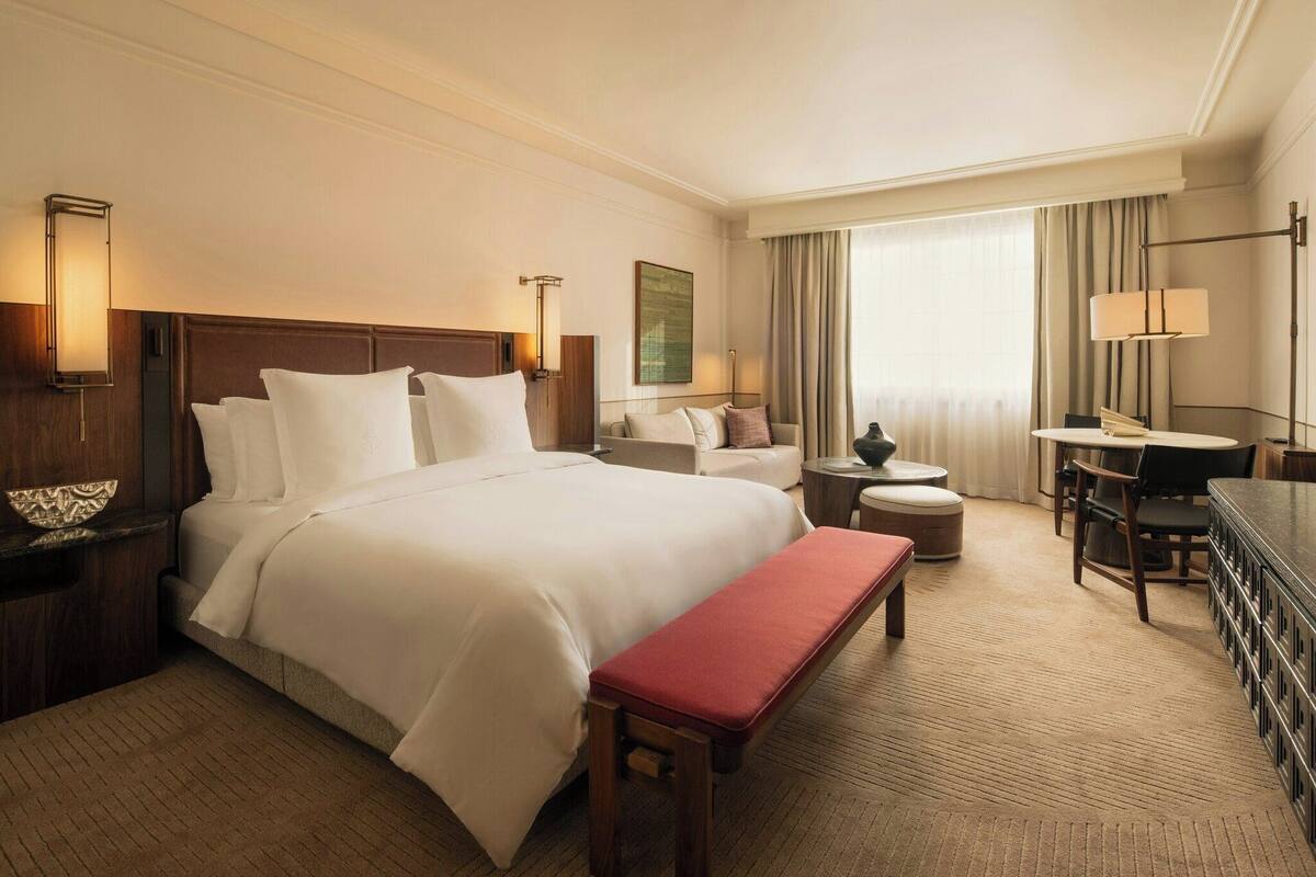 Una habitación de hotel con una cama grande, un escritorio, una silla, una mesita y un banco.