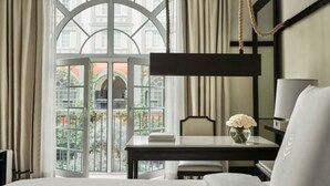 Ein Hotelzimmer mit großem Fenster, einem Bett, einem Nachttisch mit Blumenvase und einem Sessel.