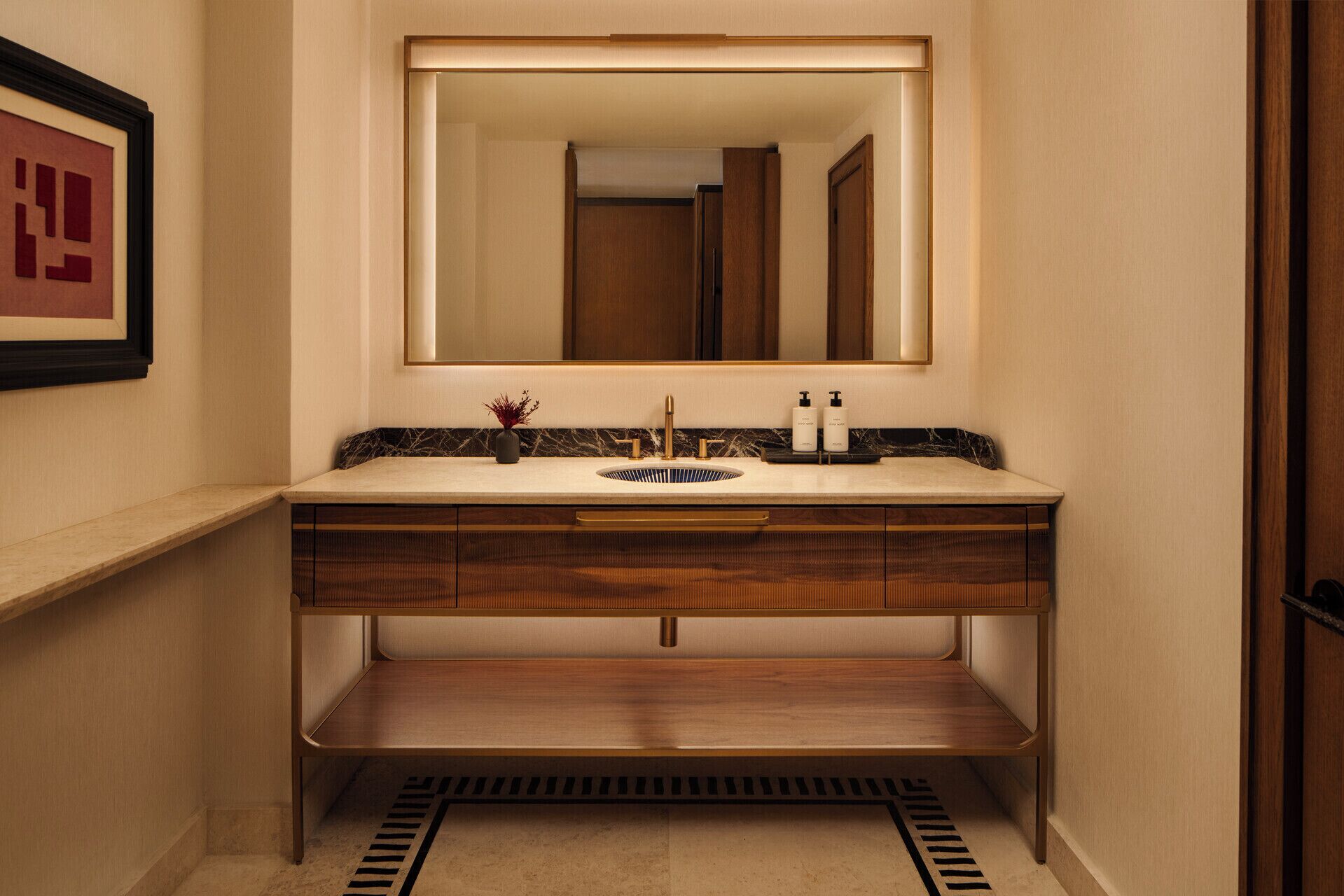 A bathroom with a marble countertop, a sink, a mirror, and wooden cabinetry.