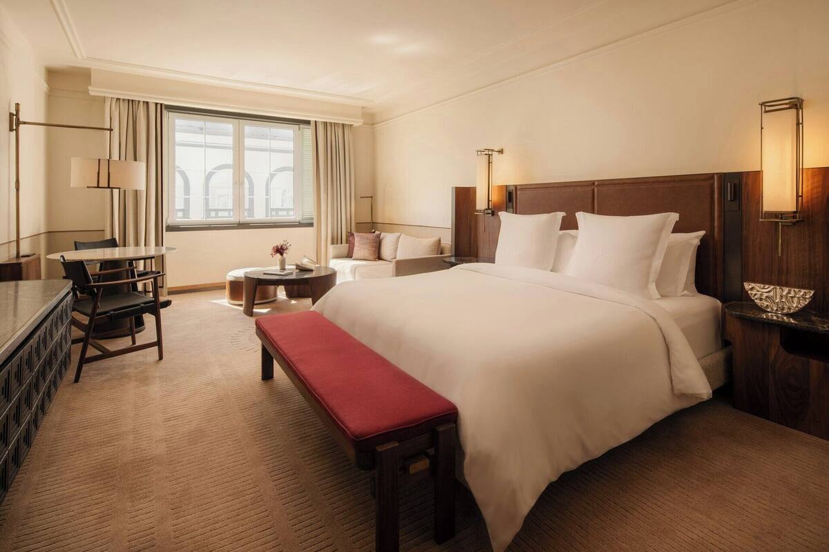 Una habitación de hotel con una cama grande, un escritorio, una silla, una mesita y un banco.