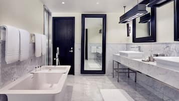 Un baño moderno con una bañera grande, dos lavamanos y una puerta oscura que da a una zona de ducha.